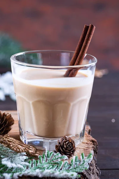 Коктейль из рождественского молока с корицей, подается в двух стаканах на деревянной доске с елкой и сосновым шишкой на темном деревянном фоне — стоковое фото