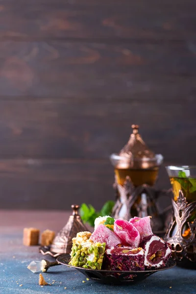 Bowl with various pieces of turkish delight lokum and black tea with mint on a dark background. — Stock Photo, Image