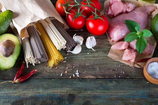 Sekelompok spageti Italia, mie soba dan sommel, daging ayam mentah, alpukat dengan tomat pada latar belakang kayu tua — Stok Foto