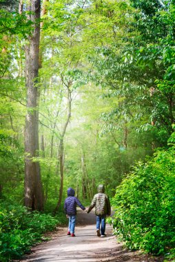 Ceketli iki çocuk güneşli bir günde güvenli bir mesafede şehir parkında ya da ormanda el ele tutuşuyorlar.