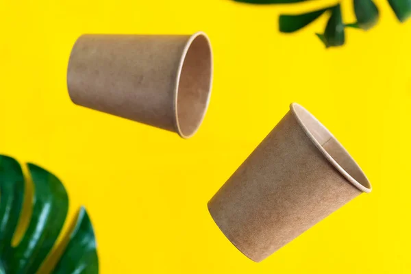 Tazas desechables de papel ecológico flotante sobre fondo amarillo con hojas de palma verde. Residuos cero — Foto de Stock