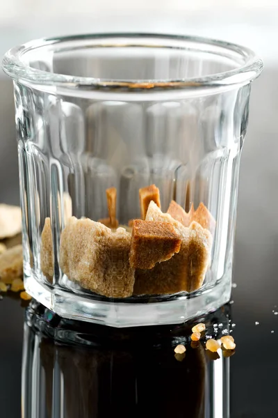 Close up glass with brown cane cubes on a dark background with reflection. — Stock Photo, Image