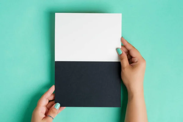 As mãos das mulheres estão segurando uma folha de papel preto branco duotone mockup vazio para texto ou mensagem acima do fundo azul-turquesa pastel . — Fotografia de Stock