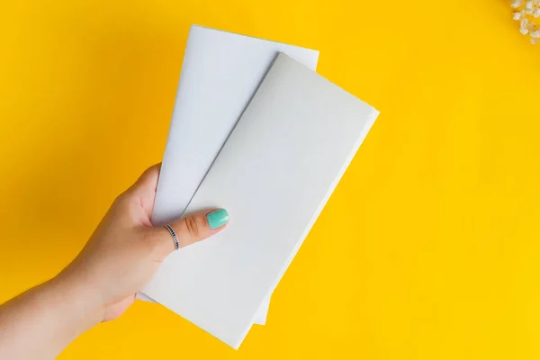 Mãos femininas estão segurando vazio brochura mock-up para escrever carta acima fundo amarelo — Fotografia de Stock