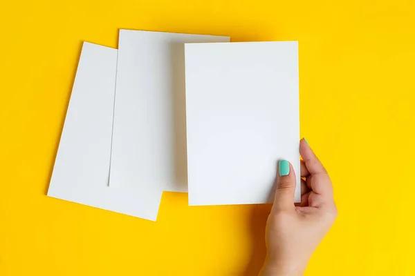 Mãos femininas estão segurando vazio brochura mock-up para escrever carta acima fundo amarelo — Fotografia de Stock