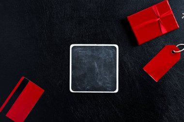 Farklı şeylere sahip yaratıcı bir zemin. Satış etiketi, kırmızı güncel kutu, siyah deri arka planda sahte kredi kartı ve kare karton, kopyalama alanı. Üst Manzara. Kara Cuma Satışı konsepti.
