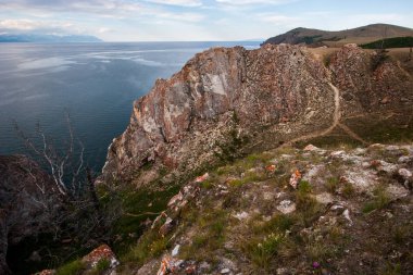 Baykal Gölü kıyısında büyük bir kaya. Kayaya giden bir yol var. Kuru bir ağaç var. Pus içinde bir dağ gölünün arkasında.
