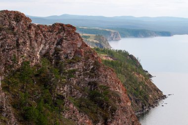 Olkhon Adası'ndaki Baykal Gölü kıyısındaki güzel kırmızı kayalar. Sis in kayalık sahile bırakarak. Ağaçlarla büyümüş kayalar.