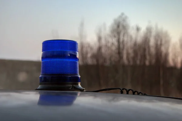 Disabled blue flasher on the roof of the car. From the flasher stretches the wire. Against the sky and blurred trees. Evening.  Selective focus.