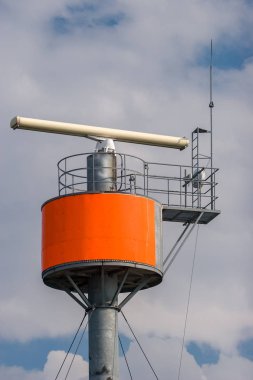 Gökyüzüne karşı yuvarlak çelik bir sütun üzerinde verici ile Radar. Gökyüzü bulutlarında. Gergin kablolar bir direği tutar.