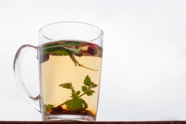 Bitkisel çay ile hala hayat bardağı. Arka planda beyaz gökyüzü. Çilek yaprakları ve çilek fincan yüzen. Yan görünüm.