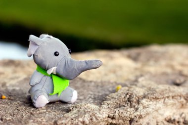Bir izci olarak yeşil kravat bir oyuncak fil bir taş üzerinde oturur. Yumuşak oyuncak. Metin için yer. Seçici odak. Arka plan bulanık.