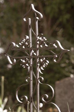 Mezarın yanında eski ferforje haç. Bulanık yeşillikli yeşil arka plan. Haça seçici odaklanma.