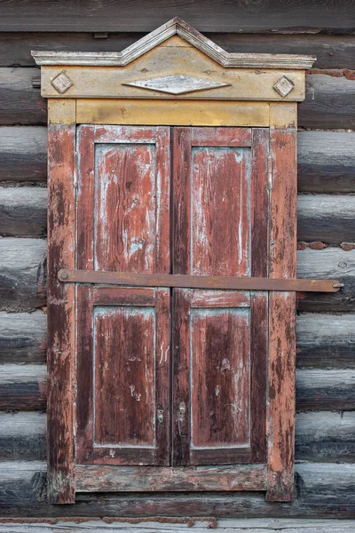 Old casement closed carved window of a house in Russian Siberia. Log house. Yellow with red color of the window. Vertical frame.
