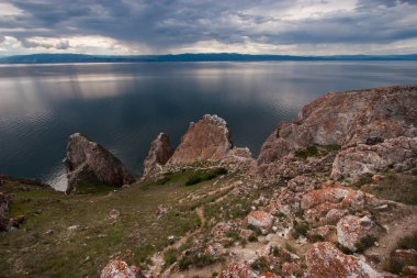 Baykal Gölü'ndeki Olhun Adası'ndaki Üç Kardeş Kayası. Gölün arka planında kocaman taşlar var. Suda, gökyüzünün güzel bir yansıması. Dağ gölünün arkasında. Bulutlarla gökyüzü.