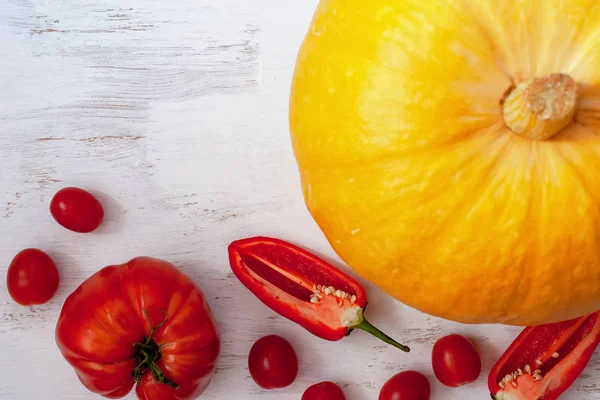 Flat view. Big pumpkin, big red tomato, sliced red pepper and small tomatoes on a light background. Suitable for decorating the menu of restaurants. View from above. Place for text.