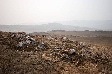 Sisli bir sabah tepe ve taşile bozkırda Ay manzara. Gri gökyüzü. Yerde ki eski çimenler. Taşların etrafında ve üzerinde kırmızı yosun var. Kopyalama alanı.