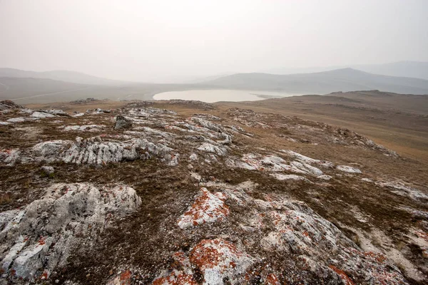 Beautiful steppe landscape with stones, hills and a lake in the fog in the morning. Red stones with moss. Like a lunar landscape. Copy space.