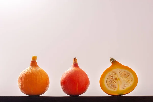 One red pumpkin, one yellow and one cut with seeds inside, lie in a row against a white background. Red pumpkin in the center. Copy space.