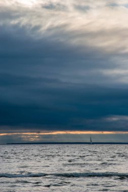 Güzel bir deniz manzarası, ağır bulutlar ve küçük bir yat. Rüzgarlı, kasvetli, küçük dalgalar. Dikey çerçeve.