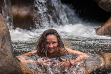 Doğal bir şelalenin suyunda gülümseyen ve kameraya bakan hoş bir kız. Seçici olarak kıza odaklan, arka plandaki düşen su bulanıklaşıyor..