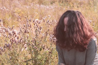Yaşam tarzı. Saçları yüzüne dökülen üzgün, deli bir kız. Depresyon. Sonbahar bunalımı. Seçici bir şekilde kıza odaklan. Arka plandaki çimenler bulanık..