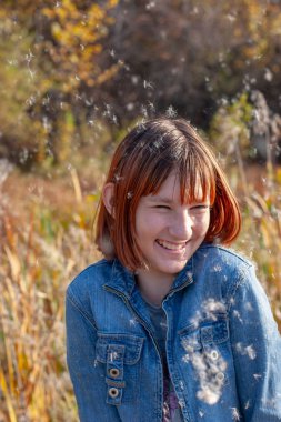 Neşeli, mutlu bir kız etrafta sinekkuyruğundan güler ve kabarık tüyler saçar. Seçici bir şekilde kıza odaklan. Sonbahar ormanı ve bulanık bir arka planda kabarcıklar. Dikey.