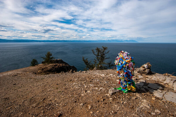 View of Lake Baikal from a cliff with a bunch of ribbons on a cliff on a sacred place on the island of Olkhon. Clouds in the sky. Behind the mountain lake. Sunny weather.