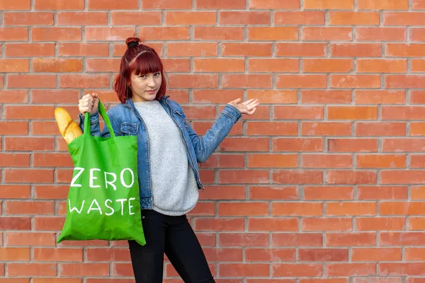 Textile bag zero waste in a girl\'s hand on a background of a brick wall. French bread in a bag. Copy space on the right.