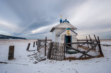 Ortodoks Rus kilisesi kışın açık alanda. Gökyüzünde güzel bulutlar. Eski, çürük çitler..