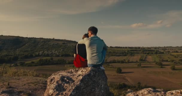 Junges Paar umarmt sich, während es auf einer Klippe mit schöner Aussicht sitzt. — Stockvideo