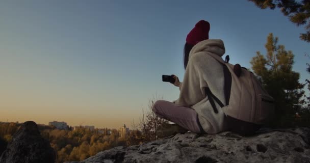 夕阳西下的时候 年轻的女性坐在悬崖上自拍 — 图库视频影像