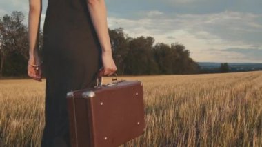 Tarlada bavul taşıyan genç bir kadın..