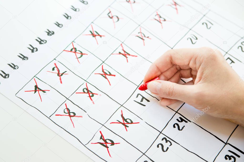 Female hand counting days in hand drawn calendar with red pastel pencil