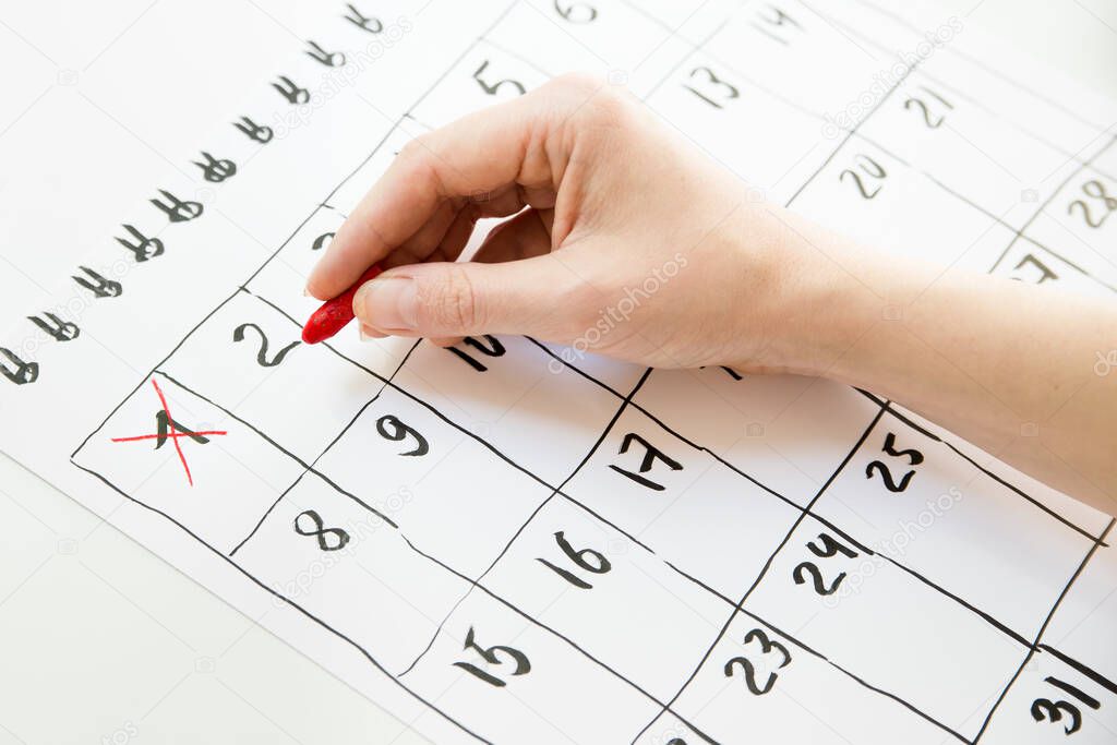Female hand counting days in hand drawn calendar with red pastel pencil