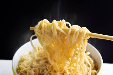 Buharlı erişteler ve siyah arka planda bir kasede duman. Masada Asya yemekleri var.