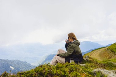 Genç bayan yürüyüşçü yürüyüş gezisinde güzel dağlarda oturur. Doğada dinlenen aktif bir insan. Kamp yapan sırt çantalı gezgin etkinleştirildi