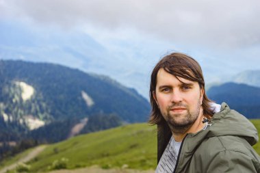 Genç adam yürüyüş gezisinde güzel dağlarda oturur. Doğada dinlenen aktif bir insan. Kamp yapan sırt çantalı gezgin etkinleştirildi