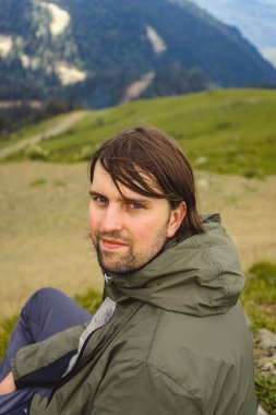 Genç adam yürüyüş gezisinde güzel dağlarda oturur. Doğada dinlenen aktif bir insan. Kamp yapan sırt çantalı gezgin etkinleştirildi