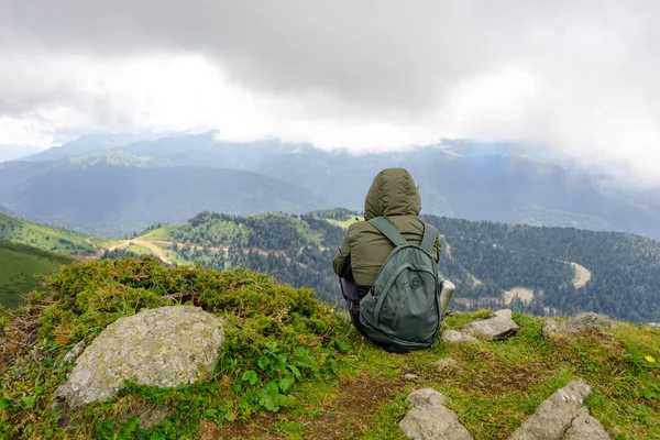 Genç adam yürüyüş gezisinde güzel dağlarda oturur. Doğada dinlenen aktif bir insan. Kamp yapan sırt çantalı gezgin etkinleştirildi