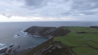 İHA 'yla bir uçurumun üzerinden uçarken, arka planda bir deniz feneri ve yolun üzerinde bir araba var. Volando sobre un acantilado con un dron, al fondo se puede ver un faro y un coche en la carretera
