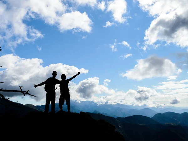 silhouette of two friends together on top of a mountain with a beautiful landscape