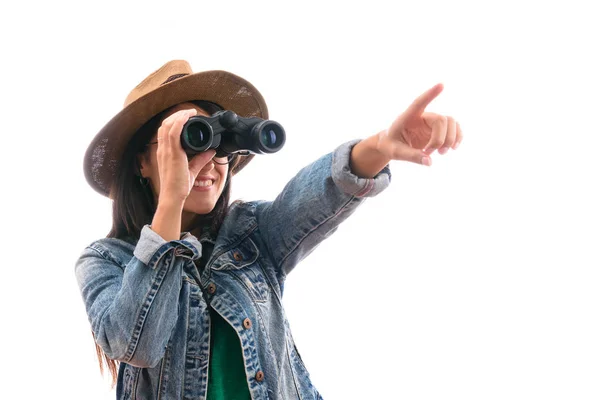 Chica scout morena vestida con chaqueta de mezclilla y sombrero, con prismáticos apuntando con el dedo y sonriendo aislada — Foto de Stock
