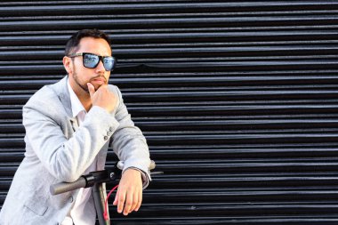 Güneş gözlüğü ile Latin yetişkin adam, iyi giyimli ve elektrikli scooter arka planda siyah bir kör ile sokakta cep telefonu konuşuyor