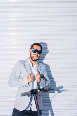 Güneş gözlüğü ile Latin yetişkin adam, iyi giyimli ve elektrikli scooter beyaz kör arka plan ile sokakta