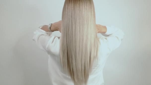 Dobře---Blondýnka, dlouhé vlasy se rozpadly na bílém pozadí. Reklama na vlasy. Krásný blonďatý pohled zezadu. Vlasy po kadeřnictví
