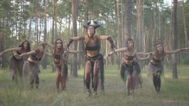 Groep vrouwelijke dansers met make-up en in mystieke fabelachtige kostuums dansen groovy dans in het bos. Forest feeën, dryaden hebben plezier onder de bomen. Prestaties van dansers buitenshuis. — Stockvideo