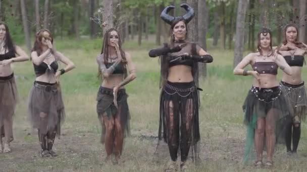 Group of women dancers with make-up and in mystical fabulous costumes dancing groovy dance in color smoke. Forest fairies, dryads have fun among the trees. Performance of dancers outdoors. — Stock Video