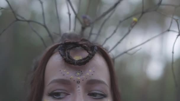 Retrato de um dryad atraente ou fada da floresta com uma coroa de ramos na cabeça e pintou o terceiro olho na testa dançando sob as árvores. Ritual antigo da criatura da floresta. Movimento lento . — Vídeo de Stock