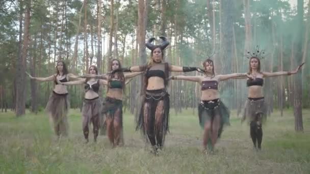 Молодые женщины в театральных костюмах лесников или дьяволов, показывающие перфоманс в зачарованном лесу и танцующие танец живота — стоковое видео